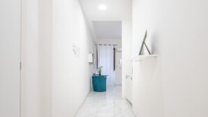 A narrow hallway with white walls and a marble floor, leading to a room with a bed and a window. - Guest Room Historic Centre (Iglesias)