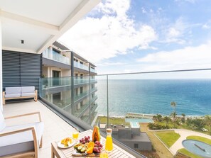 A balcony with a view of the ocean, a dining table with fruit and juice, and a sofa.