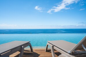 A poolside view with two lounge chairs and a clear view of the ocean.