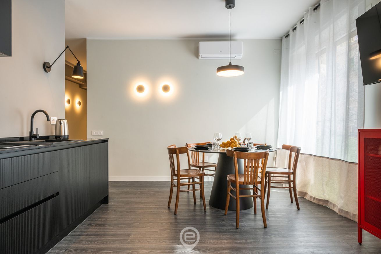 Eine moderne Küche mit Essbereich, inklusive einer zentralen Kochinsel, dunklen Schränken und einem runden Tisch mit Stühlen.