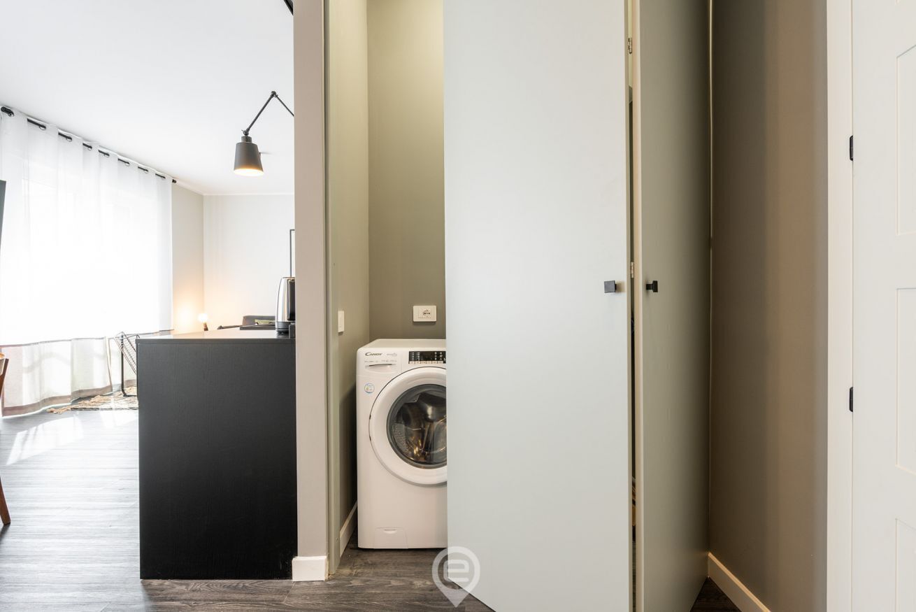 Eine moderne Wohnung mit Waschbereich, einer kleinen Küche und Blick auf den Wohnbereich.