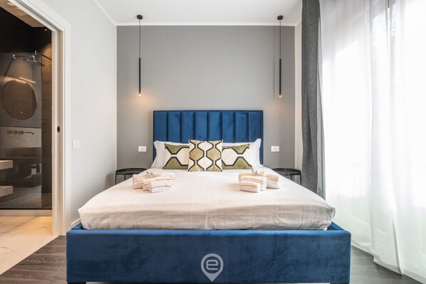 A modern bedroom with a large bed, a blue headboard, and a visible logo on the bed.