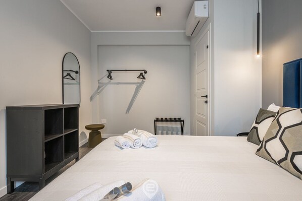 A hotel room with a bed, a wardrobe, a towel rack, and a small table.