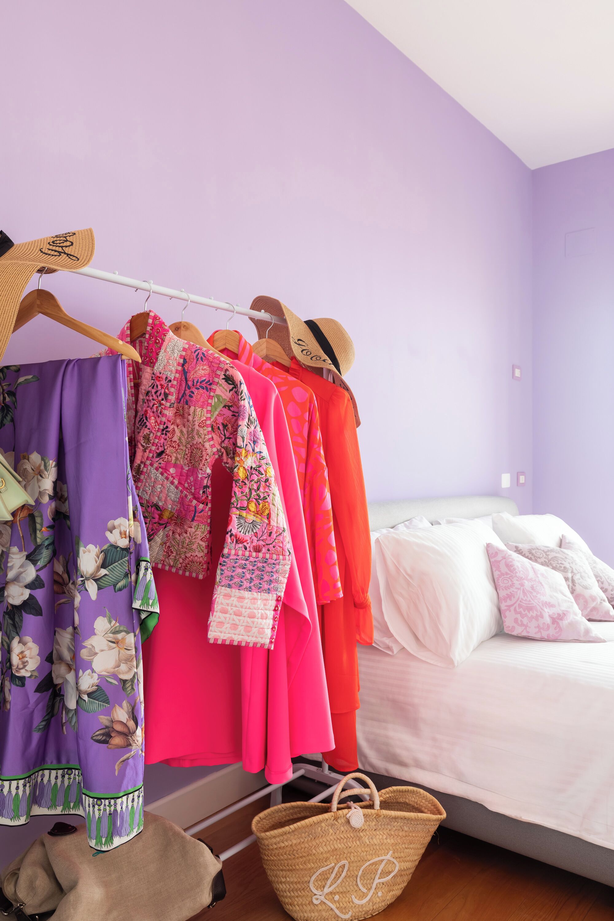A bedroom with a bed, a clothing rack with various garments, and a wicker basket.