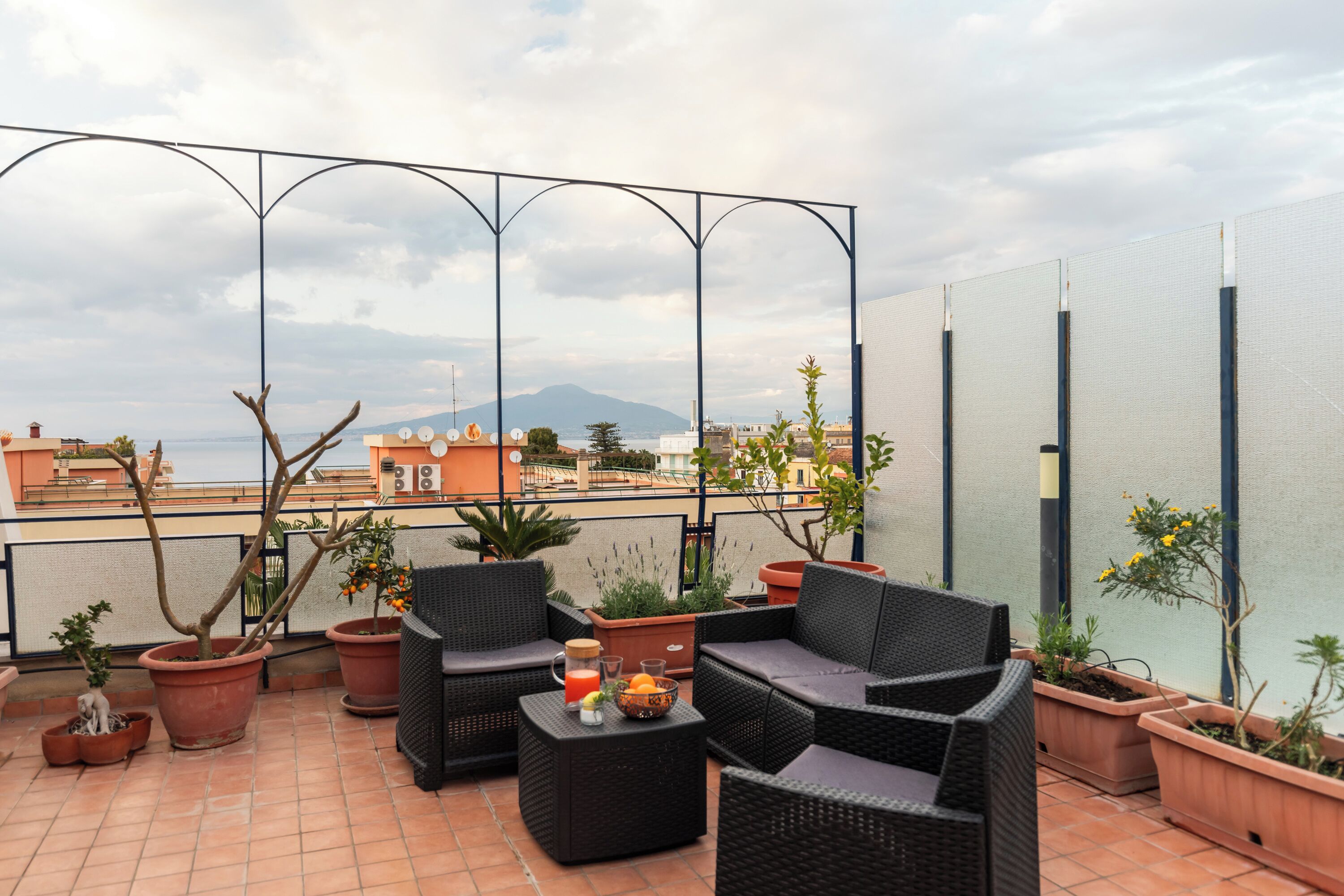 A rooftop terrace with outdoor furniture, potted plants, and a view of the cityscape.