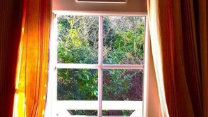 A window with a stained glass design, curtains, and a view of greenery outside.