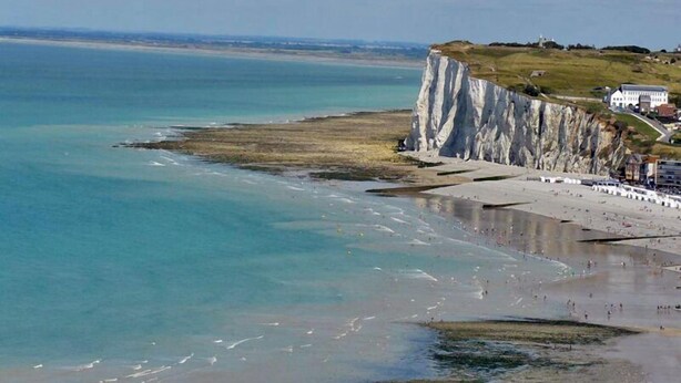 A coastal scene with white cliffs, a beach, and a building on the cliffside.