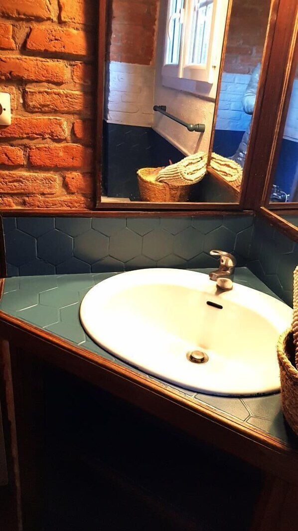 Un baño con un lavamanos blanco, un espejo con marco de madera y salpicaduras de azulejos hexagonales.