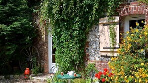 A garden with a brick wall, a green table with chairs, and a red frog statue.