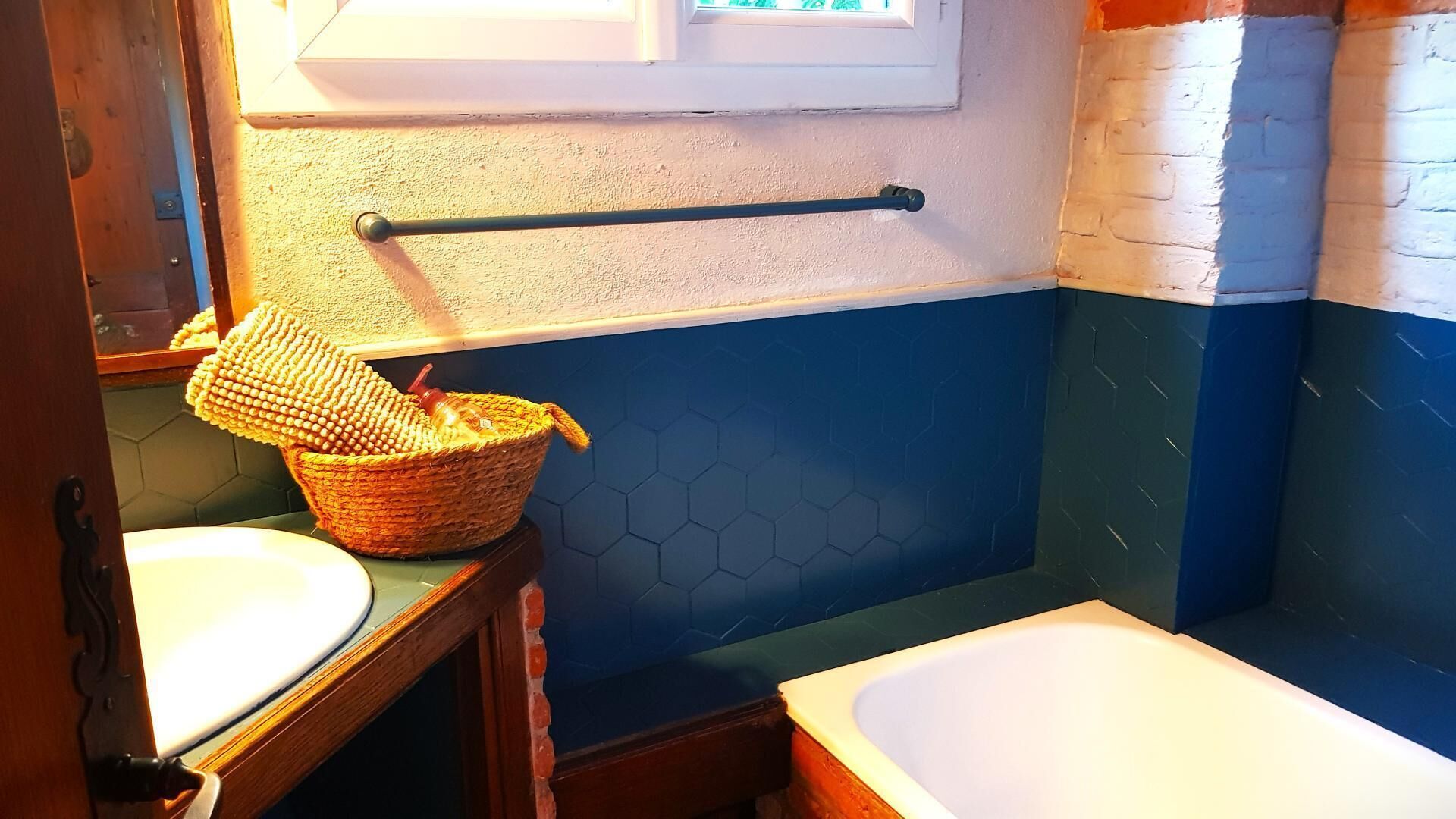 A bathroom with a wooden vanity, a white sink, a wicker basket, a towel rack, and a blue and white tiled wall.