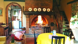 A cozy room with a brick fireplace, a dining table, and a wicker chair.