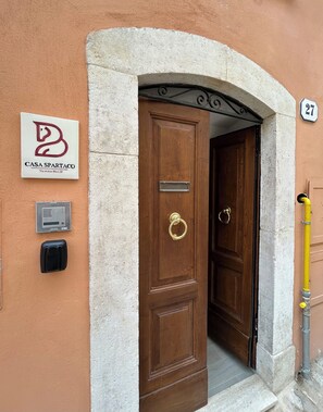 A wooden door with a brass knocker, a mailbox, and a sign for 'Casa Spartaco' on the wall.