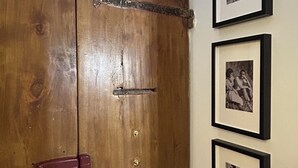 Une porte en bois, dotée d’un loquet métallique et d’une petite poignée rouge. À côté de la porte, on peut voir trois photographies en noir et blanc encadrées accrochées au mur.