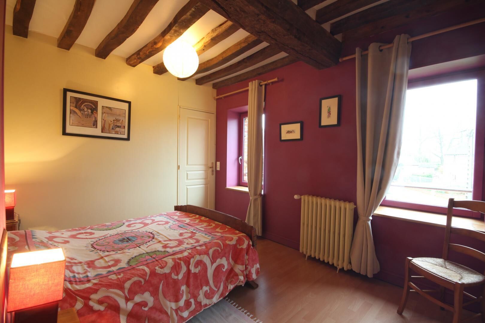 A bedroom with a bed, a chair, a radiator, and a window with curtains.