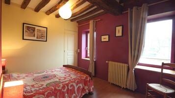 A bedroom with a bed, a chair, a radiator, and a window with curtains.