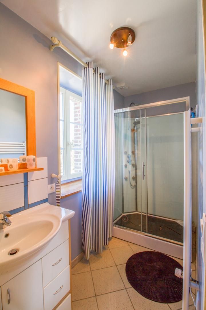 Une salle de bain avec une douche à parois de verre, un lavabo avec un miroir et une fenêtre avec des rideaux.