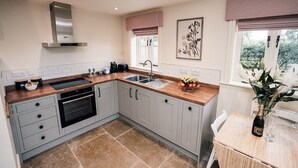 A modern kitchen with grey cabinets, a wooden countertop, a stainless steel range hood, a built-in oven, a sink, and a window with a view of greenery. - Luxury Farm Cottage with Hot Tub in Yorkshire (Northallerton)
