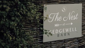 Une enseigne pour « The Nest at Sedgewell Barn », avec un fond en bois rustique et des éléments de feuillage décoratifs.