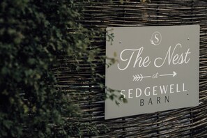 Une enseigne pour « The Nest at Sedgewell Barn », avec un fond en bois rustique et des éléments de feuillage décoratifs.