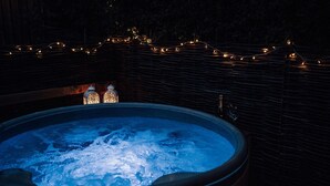 A hot tub with a wooden edge, surrounded by a stone wall, and illuminated by string lights. - Luxury Farm Cottage with Hot Tub in Yorkshire (Northallerton)