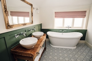 A bathroom with two sinks, a freestanding bathtub, a large mirror, and a window with a patterned valance.