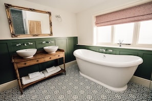 A bathroom with a freestanding bathtub, two sinks, a vanity with a mirror, and patterned floor tiles.