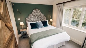 A neatly made bed with a patterned headboard, two bedside lamps, and a view of greenery through a window. - Luxury Farm Cottage with Hot Tub in Yorkshire (Northallerton)