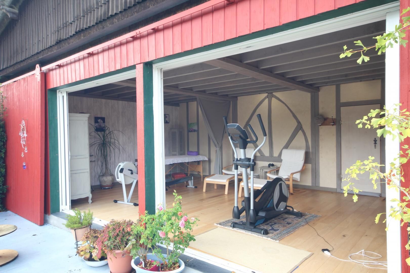 Un grand garage à l’extérieur rouge, avec une porte blanche et un espace dédié à l’entraînement, équipé de matériel de musculation.