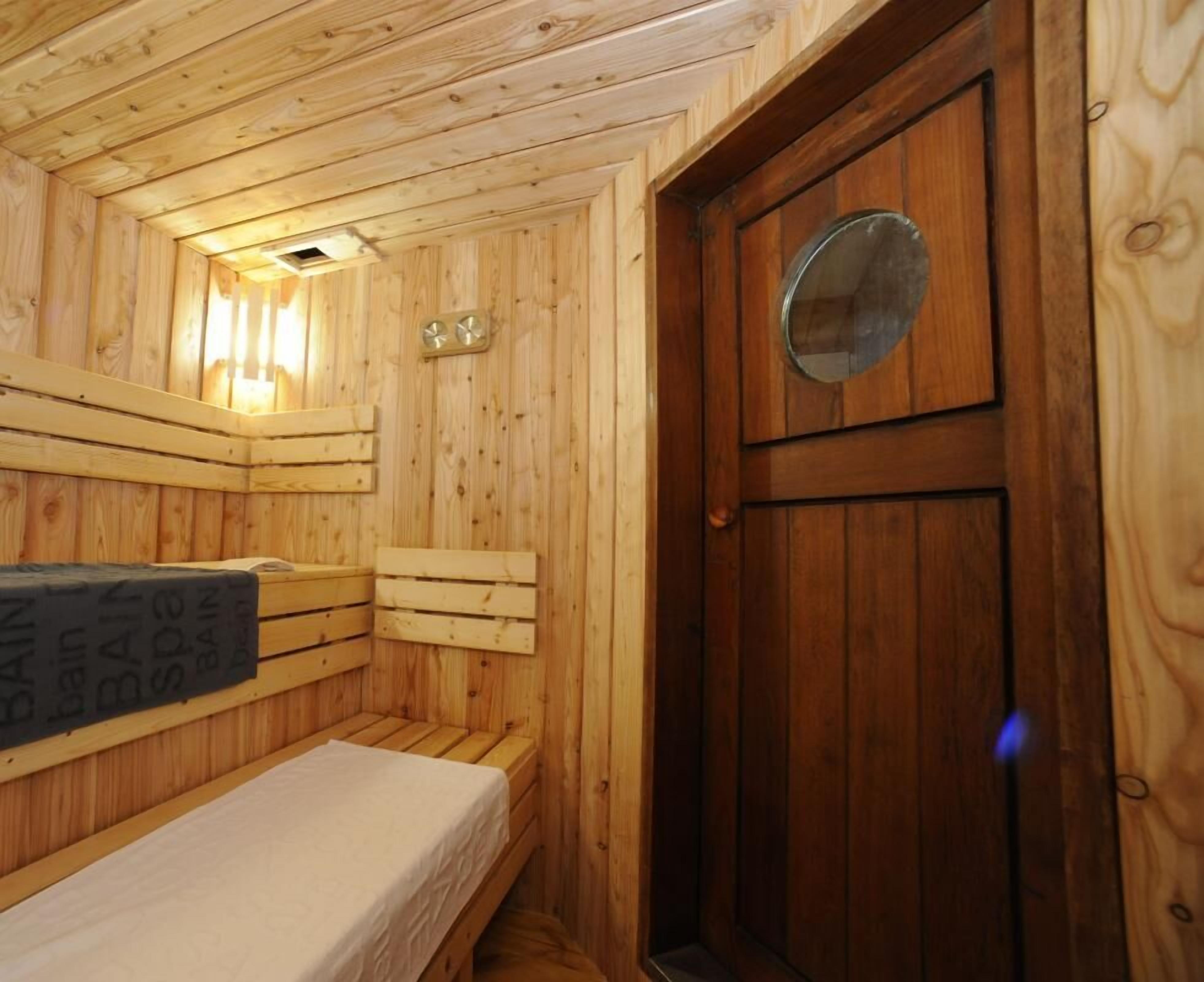 Een houten kamer met een bed, een bankje en een deur met een rond raam.