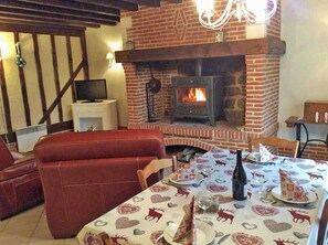 Une pièce chaleureuse avec une cheminée en briques, un téléviseur et une table à manger dressée pour deux personnes.