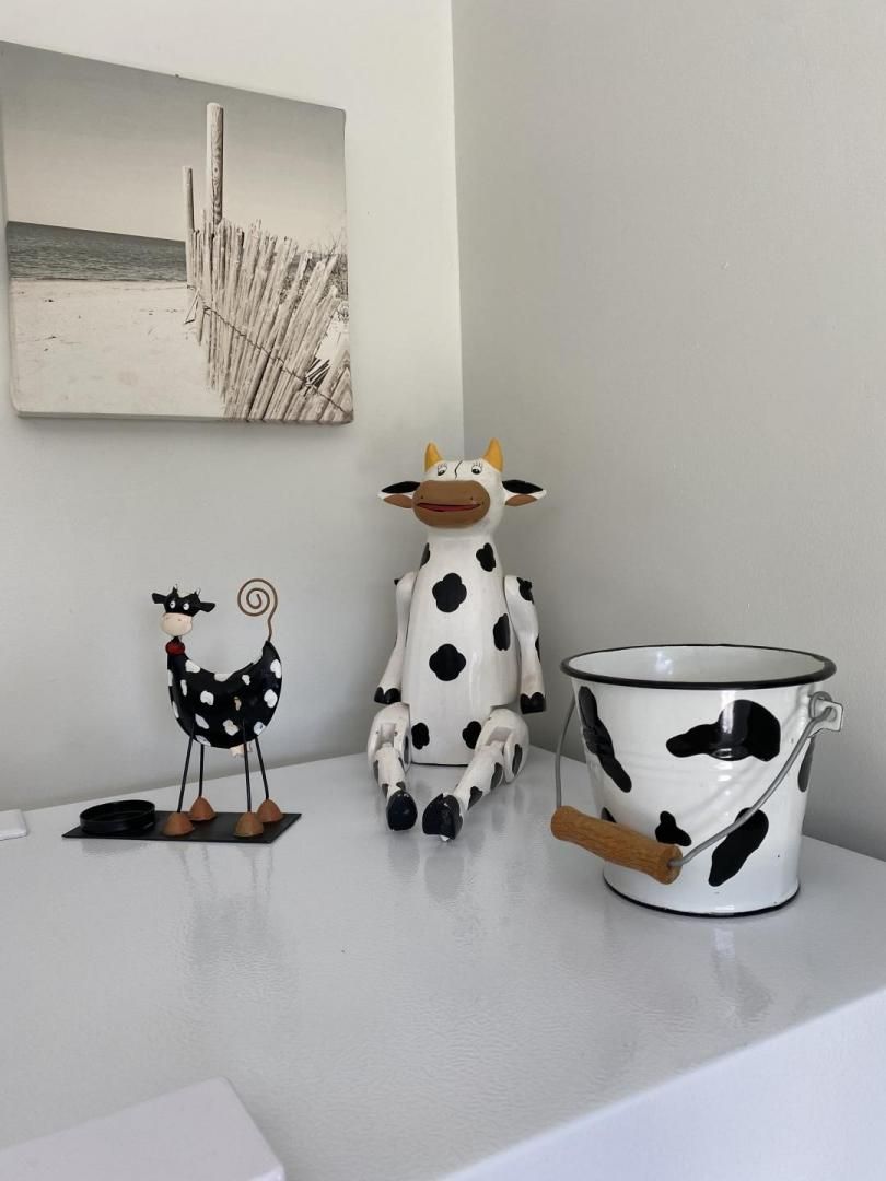 Une figurine de vache, une figurine de poulet et un pot en émail blanc orné de taches noires, le tout posé sur une surface blanche.