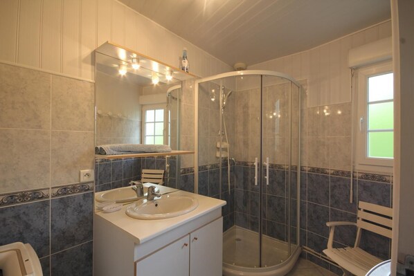 Un baño con cabina de ducha de vidrio curvo, un lavamanos con espejo y un ventanal que proporciona luz natural.