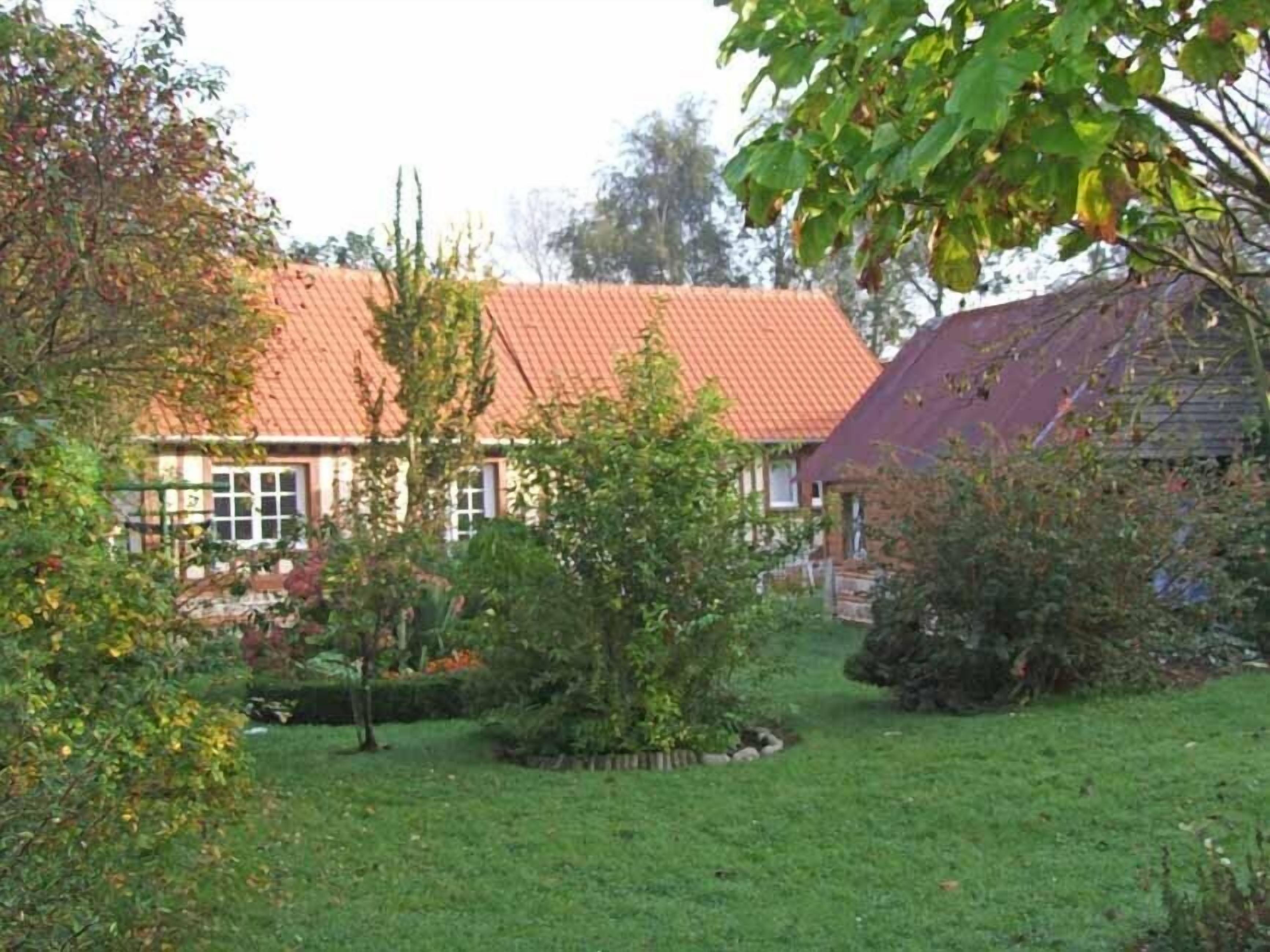 A house with a red-tiled roof, surrounded by a well-maintained garden with various shrubs and a lawn.