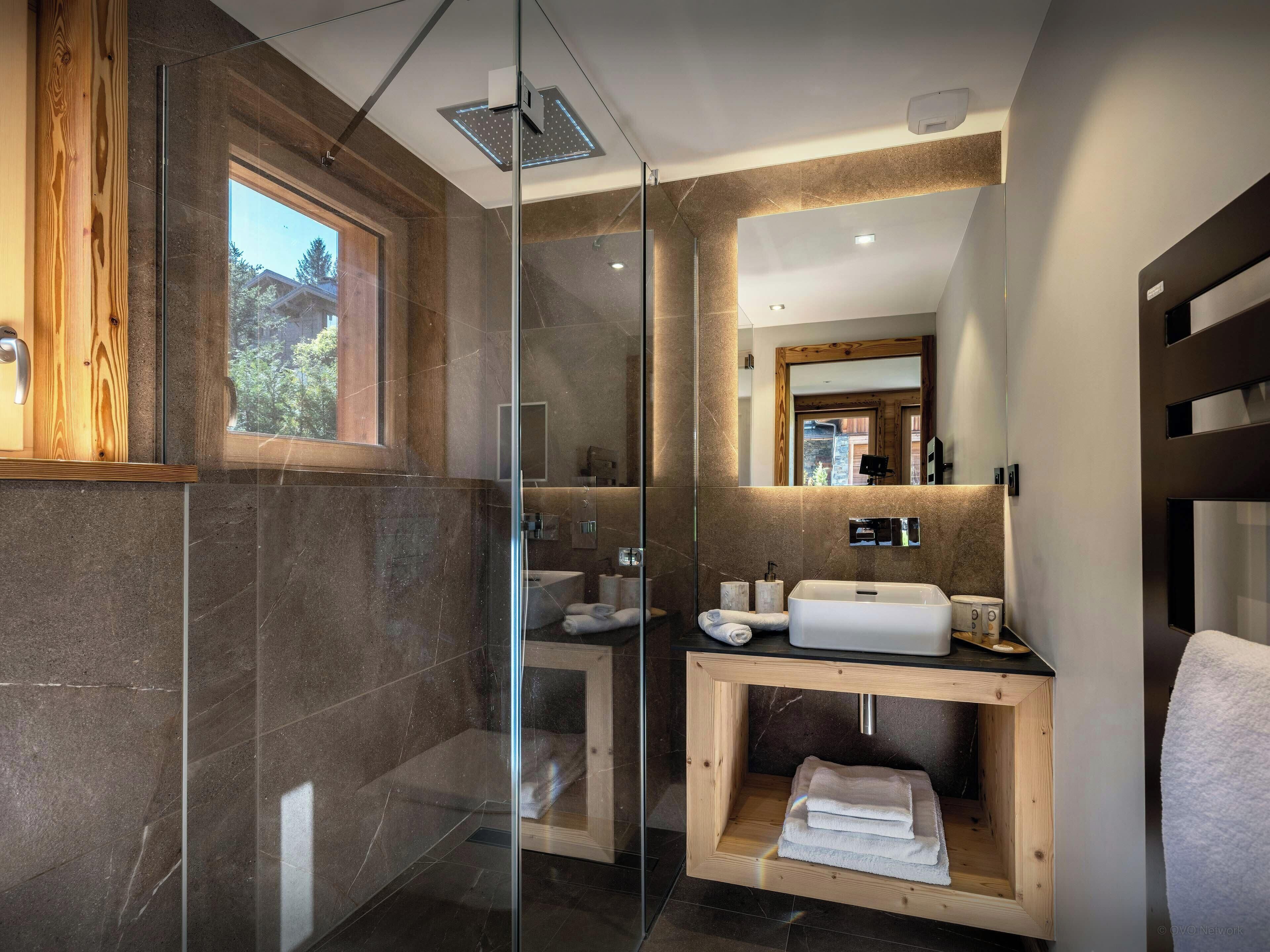 Une salle de bain moderne avec une douche à parois de verre, un meuble-lavabo en bois et un grand miroir.