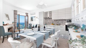 Een moderne eetruimte met uitzicht op zee, een keuken met witte kastjes en een open haard.