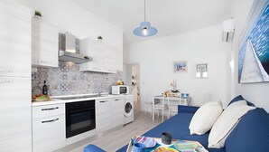 A modern kitchen with white cabinets, a microwave, and a washing machine. There is a dining area with a table and chairs, and a blue sofa with a tray of food and drinks.