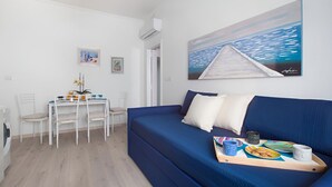 A modern room with a blue sofa, a dining table with chairs, and a painting of a pier on the wall.