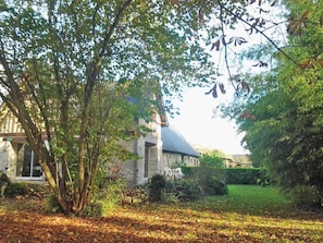 A stone building with a sloped roof, surrounded by a well-maintained garden with a lawn and trees.