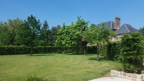 Une pelouse bien entretenue, avec un chemin de pierres menant à un bâtiment en briques surmonté d’un clocher.