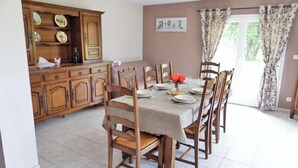 Un coin repas avec une table dressée pour six personnes, entourée de chaises en bois. On aperçoit un buffet rempli de vaisselle sur le côté gauche.