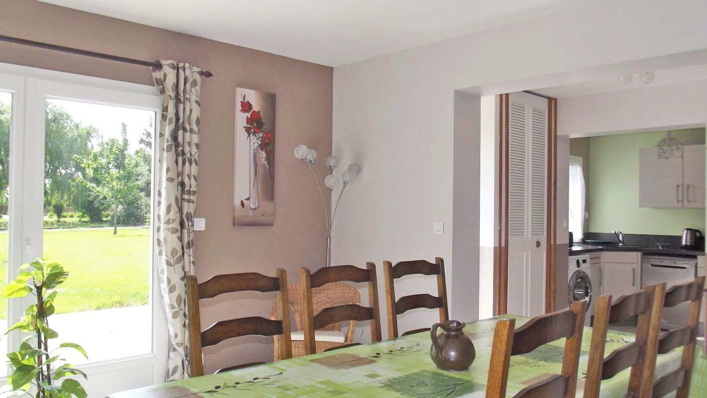 Un coin repas avec une table dressée pour quatre personnes, des chaises en bois, un vase et une fenêtre avec des rideaux.