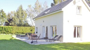 Une maison blanche avec un patio, une table, des chaises et deux transats.