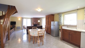 A spacious kitchen with a dining area, wooden cabinets, a refrigerator, and a built-in oven. - Gîtes de France® - L'Auge Normande (AVREMESNIL)