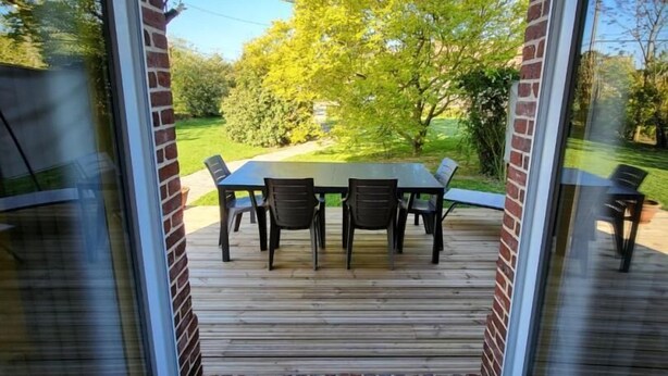 A covered patio with a table and chairs, brick walls, and a view of a green landscape. - Gîtes de France® - L'Auge Normande (AVREMESNIL)