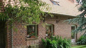 A brick house with a tiled roof, two windows with flower boxes, and a stone bench. - Gîtes de France® - L'Auge Normande (AVREMESNIL)