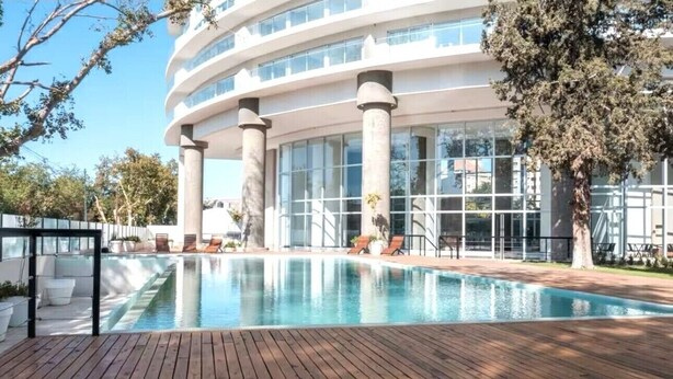 Un edificio moderno con piscina, terraza de madera y zona de estar al aire libre.