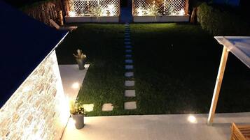 Een nachtzicht van een achtertuin met een verlicht pad, een houten terras en een kleine tuin.