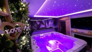 A modern bathroom with a jacuzzi, a ceiling with star-like lights, and a 'LOVE' sign.