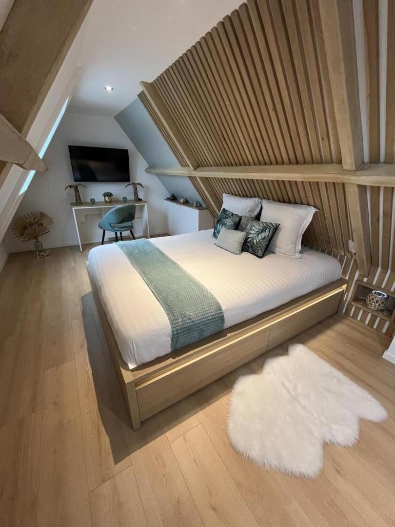 Ein modernes Schlafzimmer mit schrägem Dach, einem hölzernen Bettgestell, einem Flachbildfernseher, einem Schreibtisch und einem Stuhl.