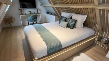 Ein modernes Schlafzimmer mit schrägem Dach, einem hölzernen Bettgestell, einem Flachbildfernseher, einem Schreibtisch und einem Stuhl.